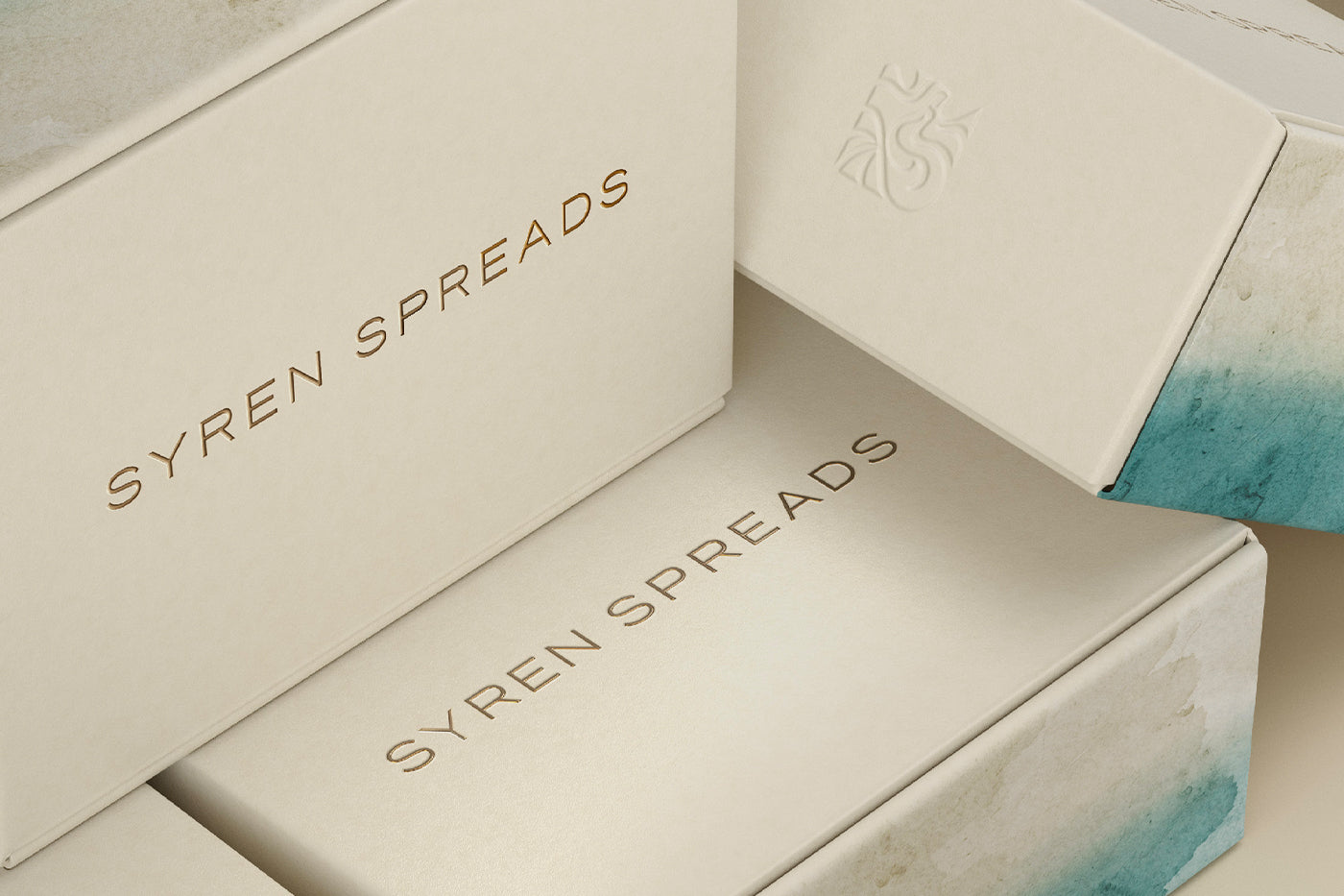 Stack of premium Syren Spreads beauty chocolate packaging boxes with embossed logo and teal accents.